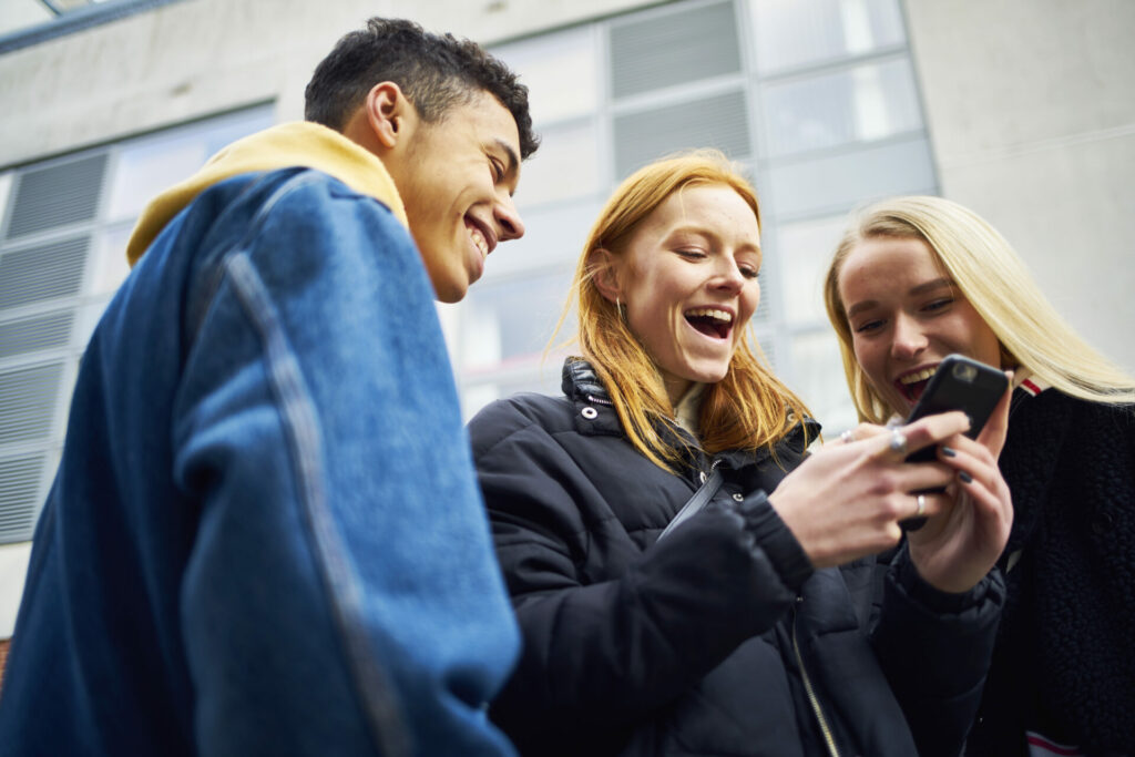 Three teens laughing and joking while looking at their phone